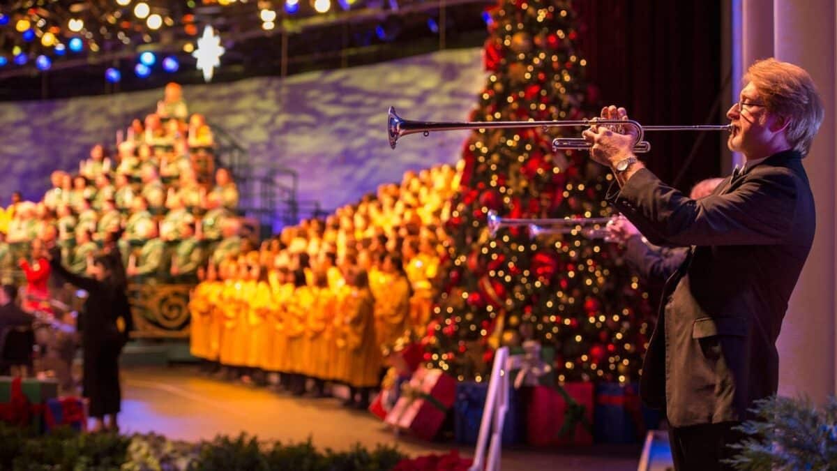 2026 EPCOT Candlelight Processional: The Stunning Show You Can't Miss 17 Performer playing bugle on stage with choir and Christmas tree behind him